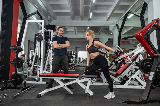 Cliente femminile in forma che si allena con un manubrio sotto il controllo del personal trainer maschile nella moderna palestra Sport come stile di vita