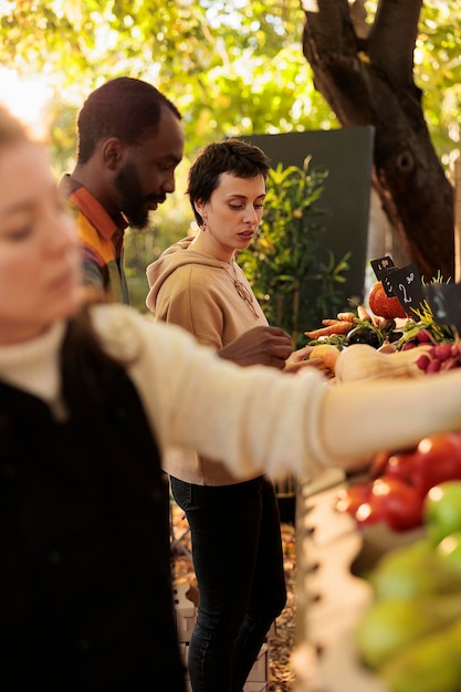 Cliente femminile sorridente che gode dell'esperienza di acquisto in fattoria al mercato locale dell'azienda agricola, donna in piedi allo stand di prodotti biologici freschi. Coppia che acquista prodotti biologici sani coltivati localmente.