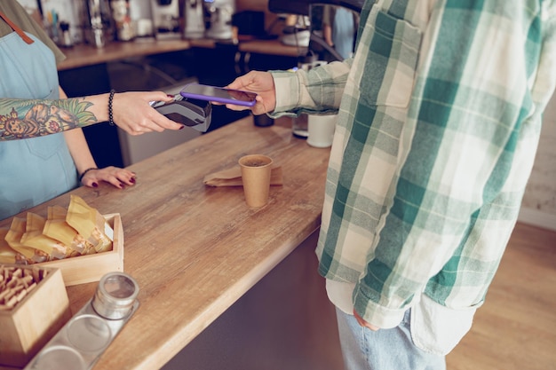 Cliente maschio che paga il caffè con lo smartphone in caffetteria