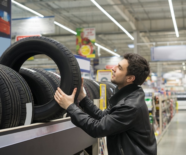 Cliente maschio che sceglie nuovi pneumatici nell'ipermercato automobilistico. Sta prendendo la gomma dallo scaffale