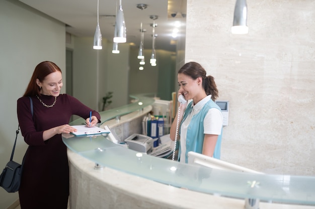 Cliente sorridente. Cliente di odontoiatria privata che sorride mentre canta documenti in piedi vicino alla receptionist