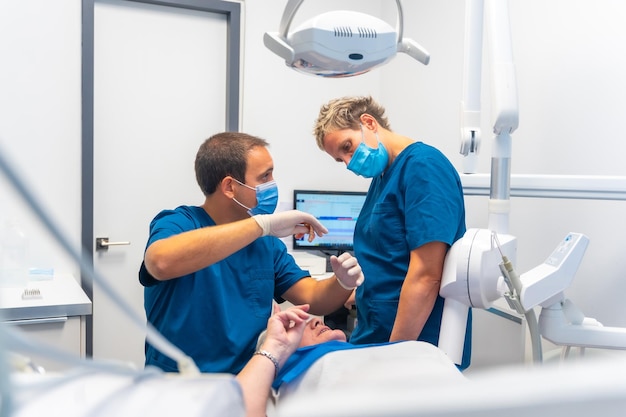 Clinica dentale dentista medico e assistente che esamina i denti di una donna anziana sdraiata sul tavolo