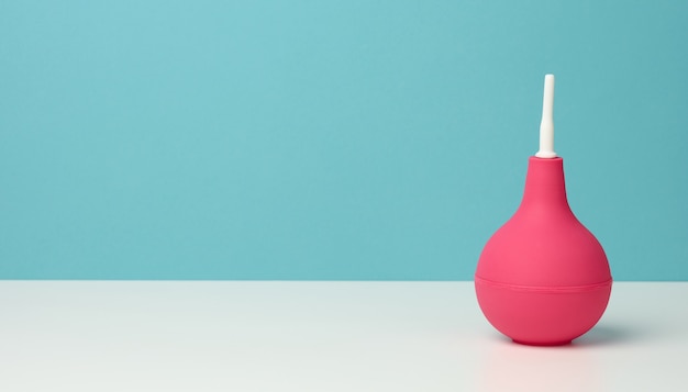 Clistere di gomma rosa sul tavolo bianco, strumento medico per la pulizia del corpo, sfondo blu, spazio di copia