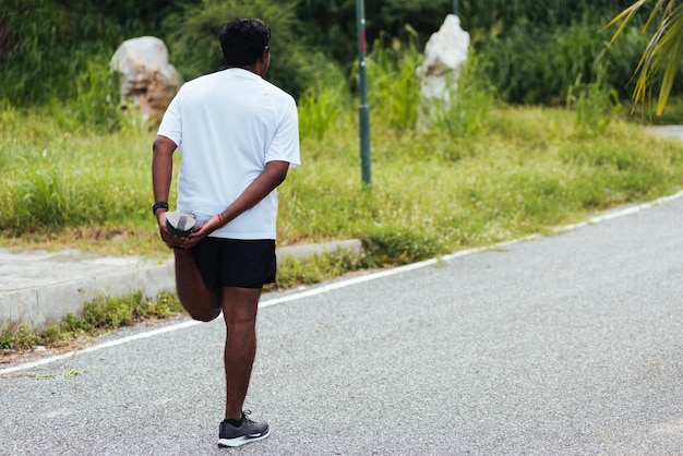 Close up asiatico giovane atleta sportivo corridore uomo nero indossare guardare sollevare i piedi allungando le gambe e il ginocchio prima di correre al parco della salute di strada all'aperto, sano esercizio prima del concetto di allenamento