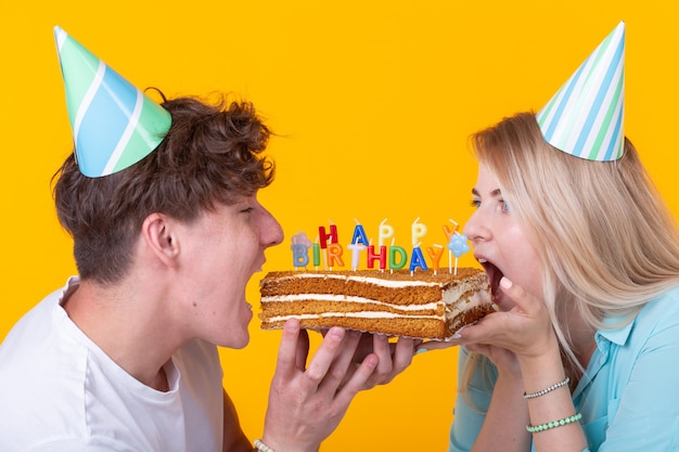 Close up bizzarro giovane coppia ragazza e ragazzo in cappelli di carta vuole mordere un pezzo di torta
