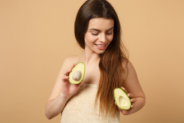 Close up bruna mezza donna nuda con pelle perfetta trucco nudo tiene avocado isolato su muro beige pastello