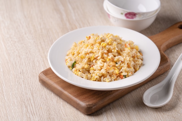 Close up cinese di riso fritto con sergestid Sakura gamberetti nel piatto bianco sul luminoso tavolo in legno