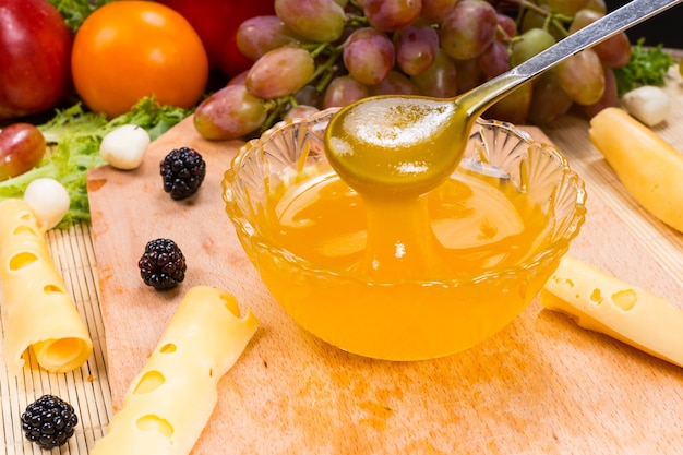 Close up ciotola di conserve di frutta con cucchiaio su tavola di legno con formaggio e varietà di frutta fresca