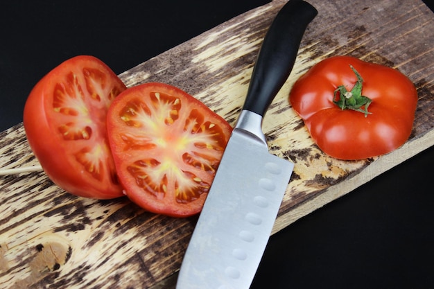 Close up coltello e pomodoro sulla tavola di legno Cottura sana mealA pomodoro tagliato in due metà con un coltello affilato