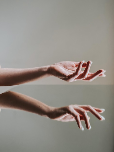 Close-up della mano di una donna contro uno specchio a sfondo grigio