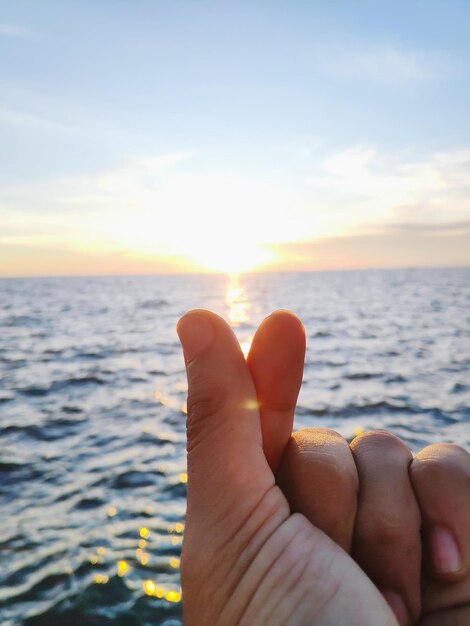 Close-up delle mani contro il mare durante il tramonto