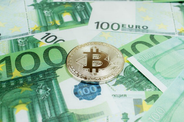 Close-up di Bitcoin monete d'argento su 100 banconote in euro. Criptovaluta BTC.