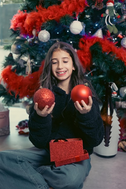 Close-up di bruna adolescente azienda casella con palle di Natale rosse su sfondo Albero di Natale
