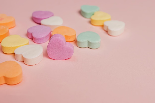 Close-up di caramelle colorate a forma di cuore su sfondo rosa pastello il giorno di San Valentino