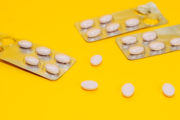 Close-up di diverse pillole e vitamine sono sparse su uno sfondo giallo, pillole in un pacchetto