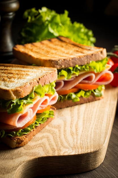 Close-up di due panini con pancetta, salame, prosciutto e verdure fresche sul tagliere di legno rustico. Concetto di club sandwich.