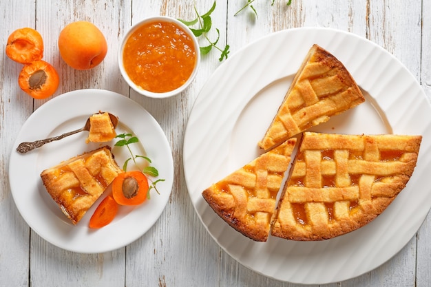 Close-up di fette di pasta frolla di albicocche torta con un traliccio di crosta di torta topping su piastre bianche su una tavola in legno rustico, piatto laici, vista da sopra