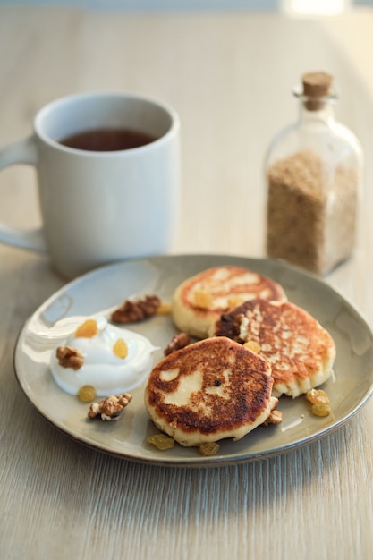 Close-up di formaggio fatto in casa pancakes syrniki con panna acida e tazza di tè