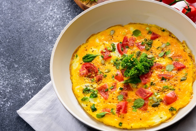 Close up di frittata con pomodori, verdure, spinaci e semi di zucca in padella su sfondo nero