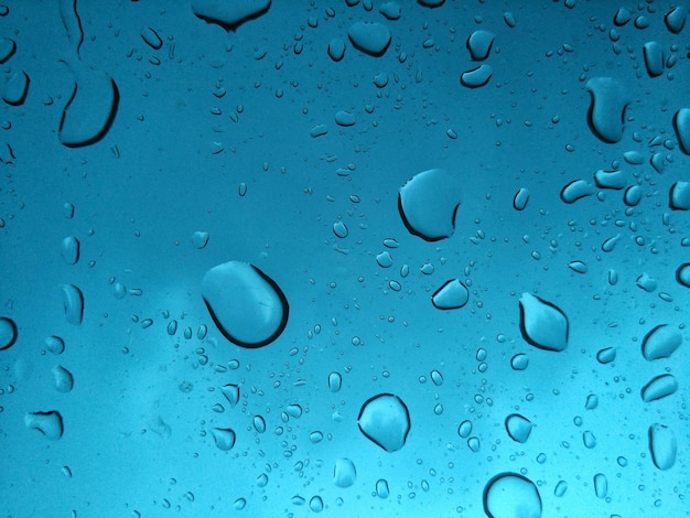 Close-up di gocce d'acqua su vetro contro il cielo blu