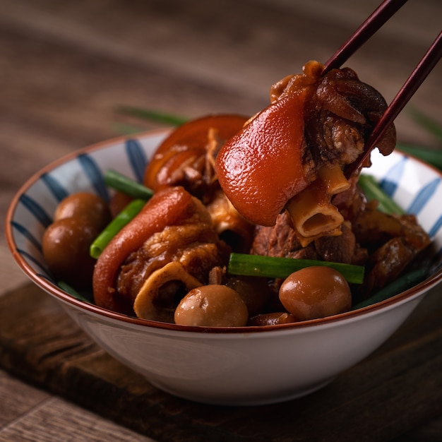 Close up di mangiare cibo taiwanese stinco di maiale in una ciotola con le bacchette sul tavolo rustico