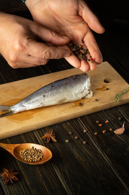 Close-up di mani di un cuoco che aggiungono pepe secco al pesce Clupea Concept di cottura di aringhe in salamoia con spezie sul tavolo della cucina