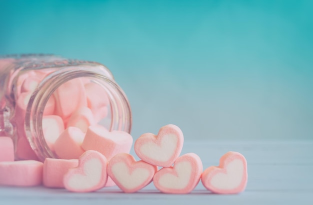 Close-up di marshmallows a forma di cuore che si riversano da un barattolo di vetro sullo sfondo blu