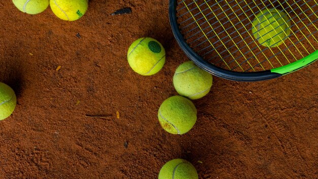 Close-up di palle da tennis verdi e una racchetta su terreno marrone