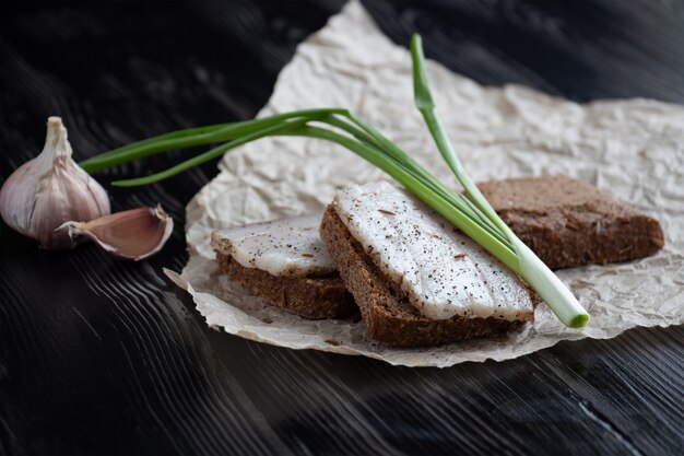 Close-up di pane nero con lardo, cipolle verdi e aglio