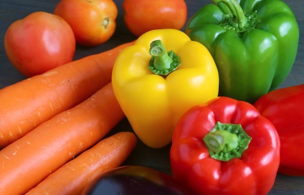 Close-up di peperoncini gialli, rossi e verdi con altre verdure fresche su uno sfondo di legno