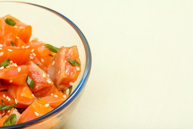 Close up di salmone hawaiano poke con cipolle verdi e semi di sesamo in una ciotola di vetro. Frutti di mare biologici. Vista dall'alto con copia spazio