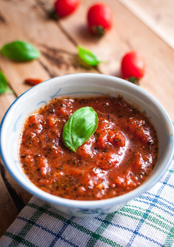 Foto close-up di salsa di pizza piccante fatta in casa con basilico fresco su un tavolo di legno