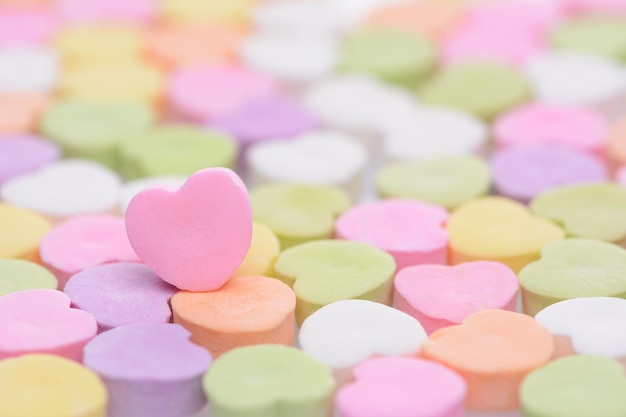 Close-up di un cuore di caramelle rosa per il giorno di San Valentino in piedi in un campo di caramele simili fuori foco Il cuore è impostato su un lato lasciando spazio per la tua copia Le caramelle sono vuote