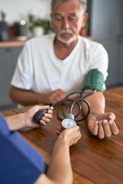 Close-up di un medico caucasico che misura la pressione di un uomo anziano in visita a casa