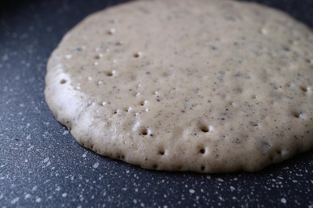 Close-up di un pancake di grano intero con semi di sesamo nero macinato che viene fritto in padella