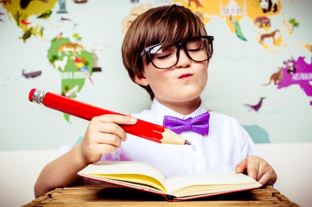 Close-up di un ragazzo carino che tiene una grande matita con un libro al tavolo