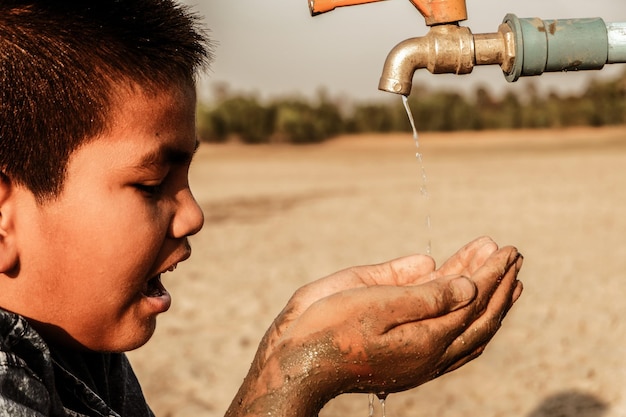 Close-up di un ragazzo che coppa le mani sotto il rubinetto che gocciola acqua