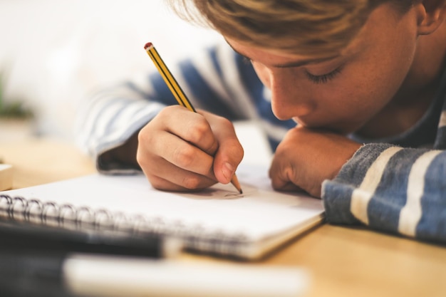 Close-up di un ragazzo che disegna su un libro sopra il tavolo