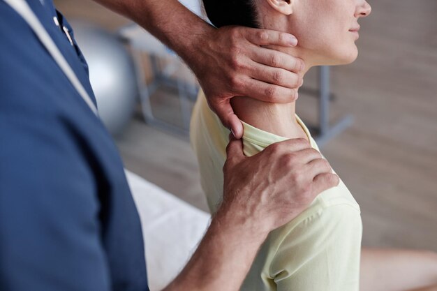 Close-up di un terapeuta manuale che massaggia il collo doloroso di una giovane donna durante la terapia in clinica