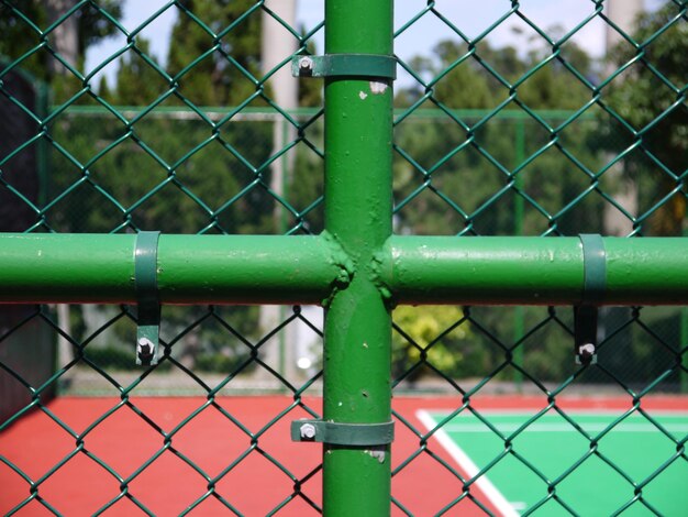 Close-up di un tubo a forma di plus su una recinzione a catena contro un campo da tennis