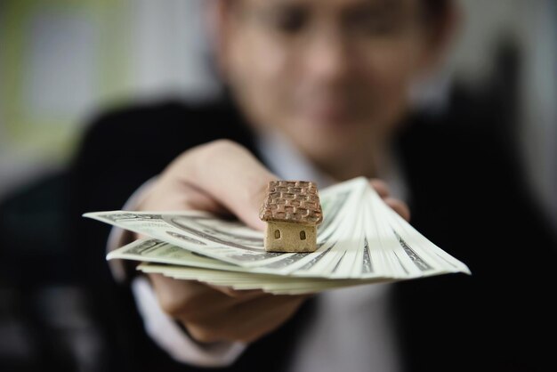 Close-up di un uomo che tiene un piccolo modello di casa e banconote