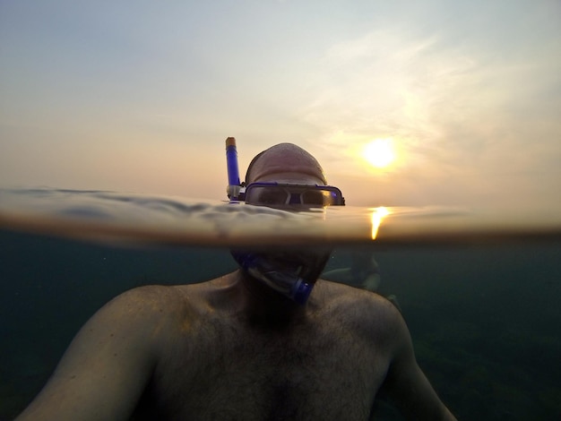 Close-up di un uomo senza camicia che nuota in mare contro il cielo durante il tramonto