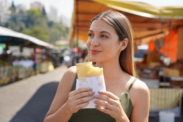 Close-up di una bella ragazza che mangia il pasto tradizionale brasiliano Pastel de Feira a Sao Paulo, Brasile