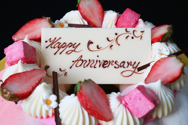 Close-up di una carta di auguri di anniversario di cioccolato bianco sopra una torta di mousse di fragole