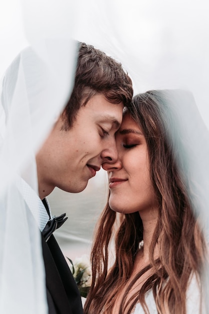 Close-up di una coppia di sposi con gli occhi chiusi che fanno l'amore sotto il velo