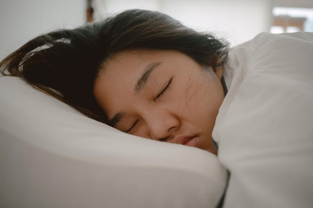 Close up di una donna asiatica thailandese che chiude gli occhi dormendo su un letto bianco al mattino in un appartamento