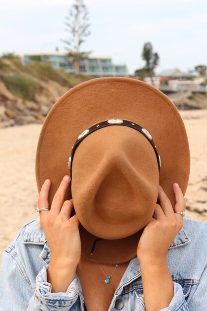 Close-up di una donna che nasconde la faccia con un cappello in spiaggia