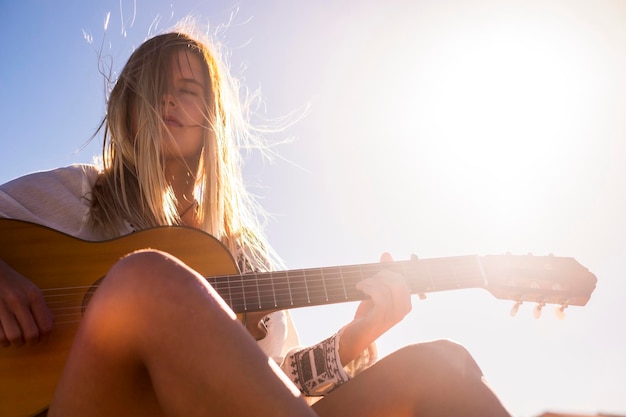 Close-up di una donna che suona la chitarra contro il cielo in una giornata di sole