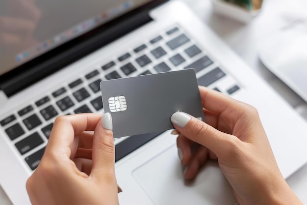 Close up di una donna con le mani che tiene una carta di credito grigia davanti a un computer portatile