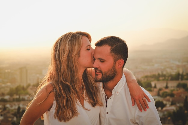 Close-up di una giovane donna che bacia un uomo contro la città durante il tramonto